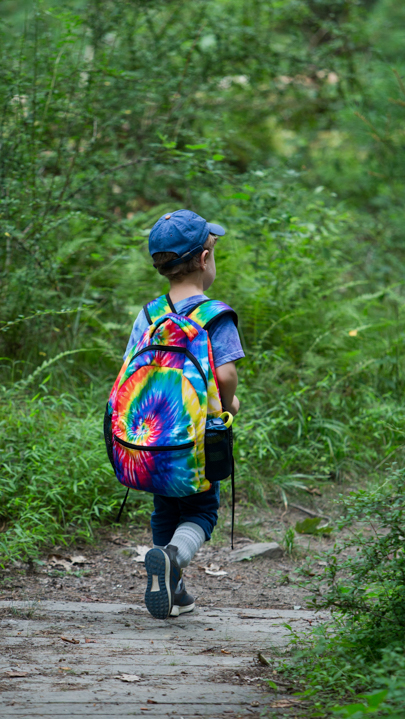 Young camper with backpack walking in the woods