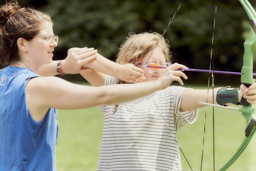Archery instructor helping camper aim bow and arrow.
