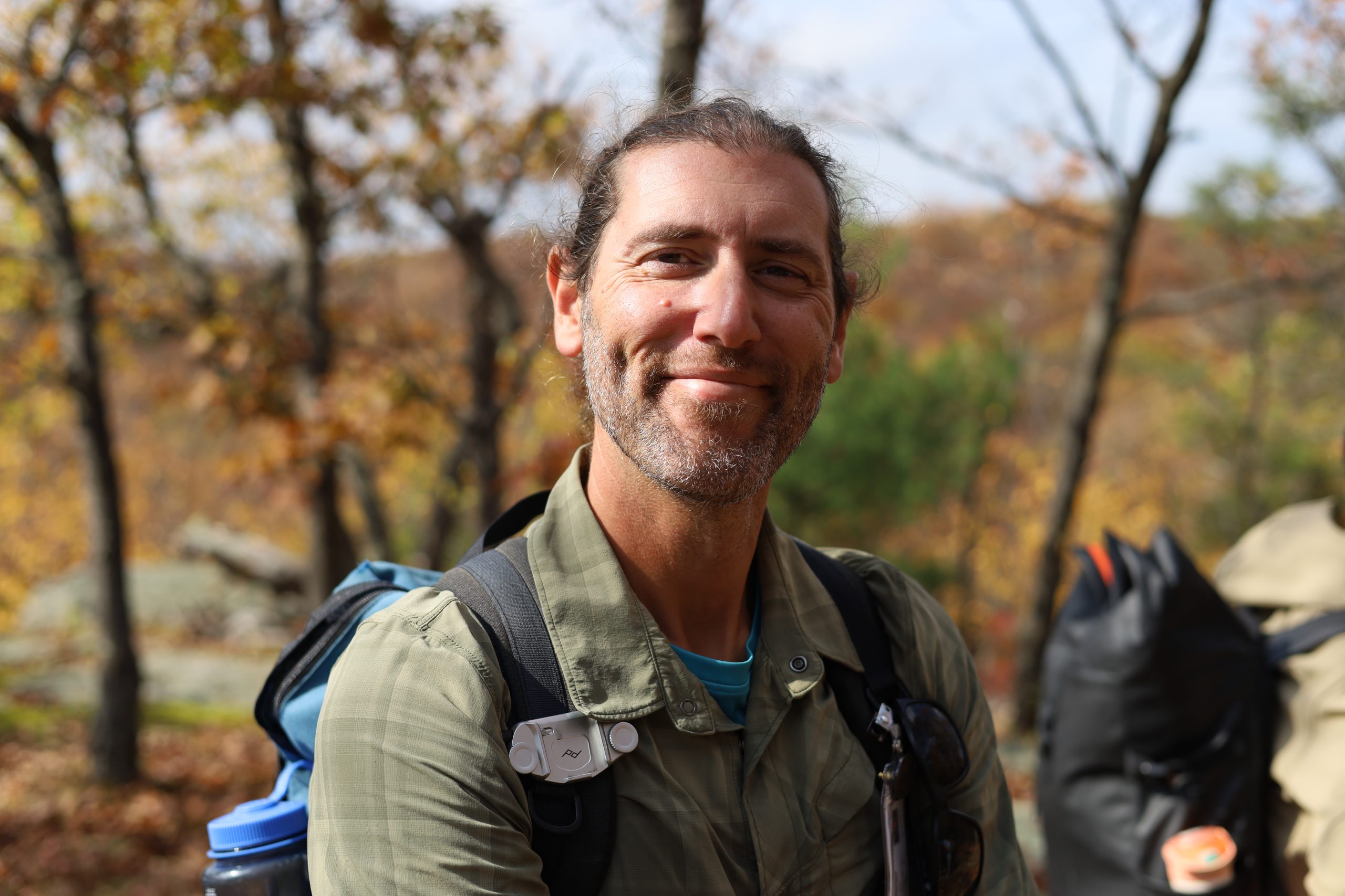 Hiker with a backpack smiling in the woods during the fall with orange and brightly colored foliage in the background