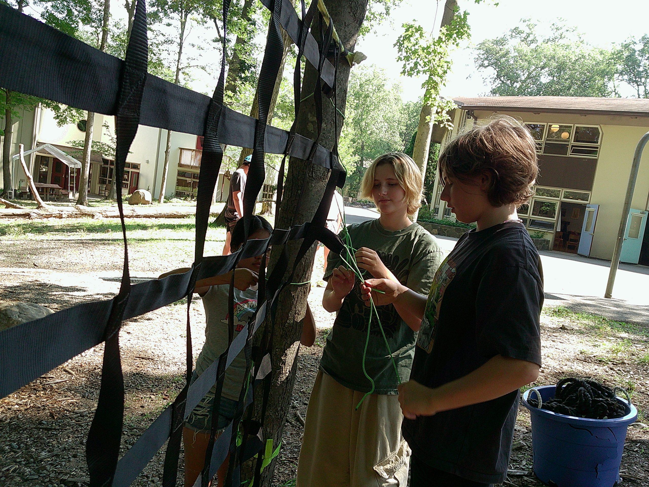 Campers tying a rope to a tree with trees in the background; non-competitive outdoor play and friendship building at The Nature Place